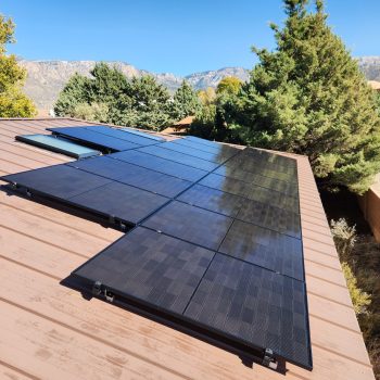 black solar panels on a metal roof with mountains in the background